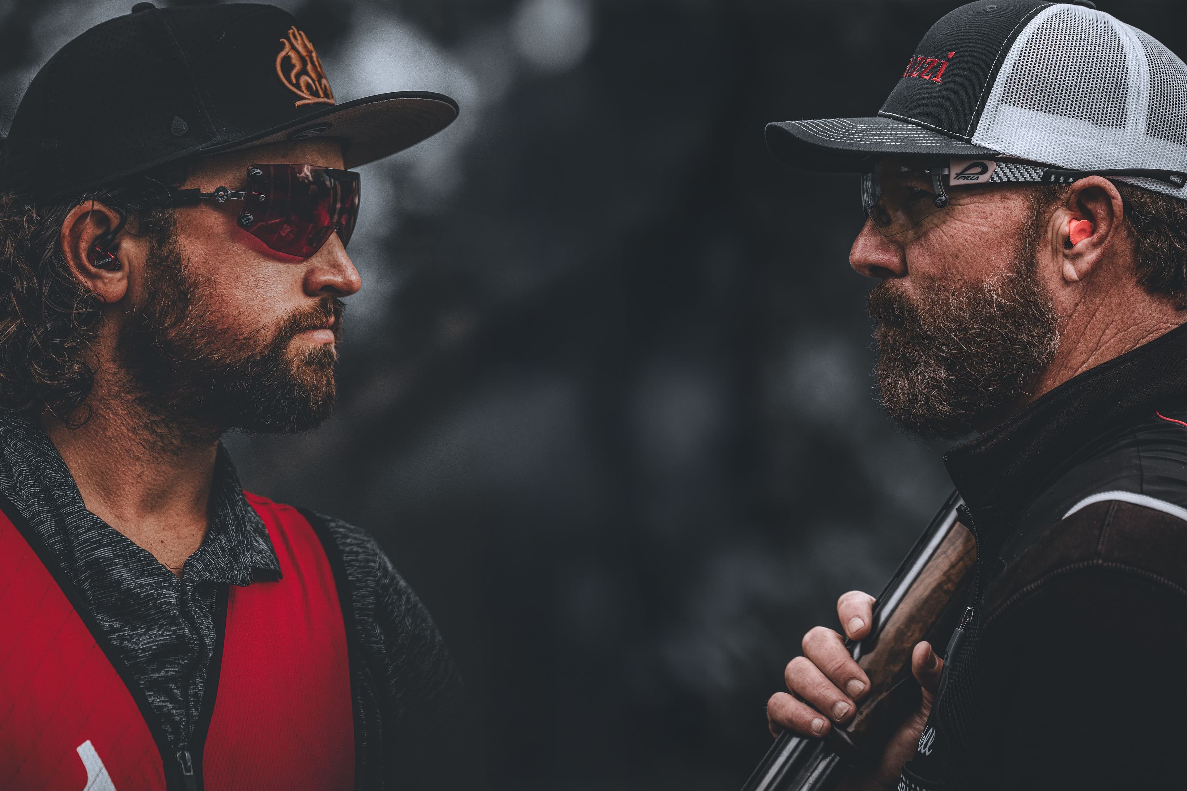 David Radulovich and Wendell Cherry face each other in focus, their expressions calm and deliberate, framed in deep shadows. One holds a Perazzi shotgun, symbolizing mutual respect and shared pursuit of mastery.